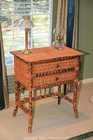 Wicker table with two drawers and two lamps on top seen by window with curtains