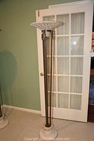 Full view of the tall torchiere floor lamp showing its height and overall structure against a green wall with a door behind.