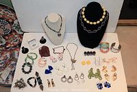 Overview of assorted costume jewelry including bracelets, rings, earrings, and necklaces laid out on white surface