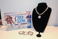 Silver Lightning silver cleaning kit box, silver braided necklace with flower pendant, two silver bracelets, and silver watch.