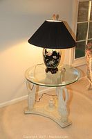 Overall view of the glass top side table and black floral lamp showing the lamp on top of the table.