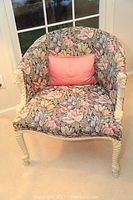 Front view of floral upholstered armchair with cream colored twisted rope and knot carved wooden arms and legs in a softly lit room by a window.