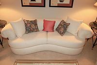Front view of white curved sofa with five pillows, showing floral and solid colors.