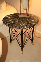 Full view of round black marble top side table with cast iron legs and brass accents.
