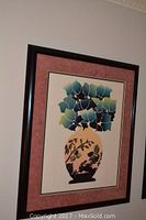 Framed fine art print by Michelle Perdue showing a stylized botanical scene with a vase and leaves, with reddish-pink mat and dark wooden frame, hung on a wall.