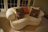 Cream upholstered love seat viewed from front with floral and plain cushions