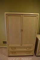 Closed front view of the Thomasville armoire showing its light cream color, two doors, and two lower drawers with brass handles.