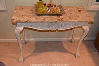 Front view of marble topped console table with carved white base and mirrored vanity tray with assorted fragrances on top.