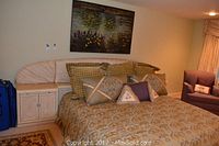 Front view of king size bed with cream curved wooden headboard and attached nightstands on both sides, bed made with gold and green bedding and decorative pillows.