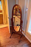 Full view of the standing floor mirror showing the wooden frame and oval mirror reflecting staircase and room elements.