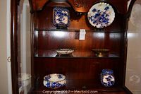 Wide shot of wooden shelves holding seven Asian themed decorative ceramics including plates, bowls, and a brass dish.