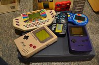 Photo of Nintendo Gameboy, Gameboy Color, and several handheld electronic games on a carpeted floor.