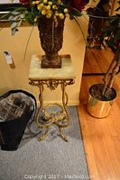 Full view of the marble top plant stand showing the square marble top and intricate gold metal base with scrollwork and claw feet design.