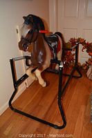 Side view of brown plastic rocking horse mounted on a black metal frame showing the red grips, saddle and mane details.