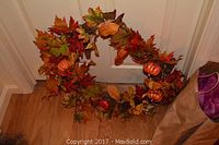 Fall wreath decorated with faux autumn leaves and miniature pumpkins on a wooden floor