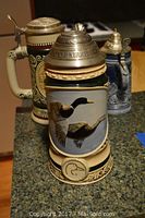 Photo of three collectible steins on counter, showing Avon Ducks Unlimited stein with flying ducks at front