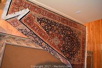 Two unrolled rugs layered on hardwood floor, showing red and navy oriental patterns.