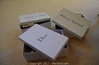 Two opened branded shoe boxes, one Manolo Blahnik and one Dior, showing the shoe boxes with logos and some contents inside.