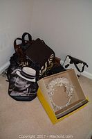 Multiple ladies purses and clutches arranged on floor corner with white flowered headpiece in a box