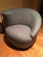 Front angled view of light gray barrel chair on swivel against wooden floor.