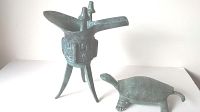 Photo showing both metal pieces: the tripod vessel with three legs and spouted top, and the turtle with textured shell.