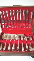 Open wooden box with red interior lining showing 13 dinner knives upright and various spoons and forks inside compartments.