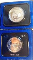 Obverse photo of two Canadian silver dollars, one Winnipeg 1874-1974 and the other P.E.I. 1873-1973, housed in blue velvet-lined protective cases.