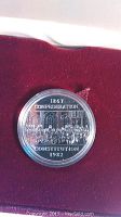 Close-up of 1867 Confederation Constitution 1982 silver dollar coin in plastic capsule on red felt interior