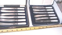 Two sets of butter knives with mother of pearl handles inside felt-lined leather-like display cases, measuring about 10 inches in length each