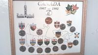 Framed display showing map of Canada with quarters pressed into the provinces they belong to, coat of arms, Parliament building illustration, and maple leaves decoration.
