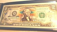 Photo of USA two dollar bill featuring Yellowstone National Park in color within a presentation binder, showing serial number and design details.