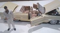 Figurine of Tony Montana standing in front of the opened door of the cream colored 1963 Cadillac Deville model with tiger-striped interior