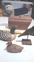 Four carved wooden ducks and decorative figures shown with a ruler and box in background