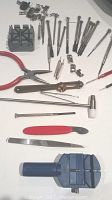Photo showing various precision screwdrivers, pliers, a blue plastic watch case holder, and small watch movement holders and clamps.
