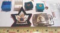 Wide shot showing the maple leaf cap medal, two service pins in blue boxes, gold pin, small white box, and silver RCMP belt buckle with crest.