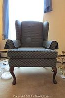 Front view of a blue patterned wing back chair with turned Queen Anne style wooden legs.