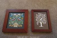 Two framed Scherenschnitte artworks showing detailed paper cuttings, one floral with birds, the other a white tree with an animal.