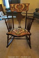 Front view of the rocking chair showing floral tapestry upholstery on seat and upper backrest with dark wooden frame and arms.