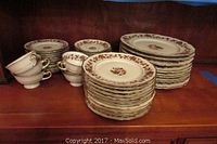 Wide view showing the stacked dinnerware including plates and cups on wooden shelf
