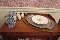Display of mugs, salt and pepper shakers, egg cups, egg plate and meat platter on wooden furniture.