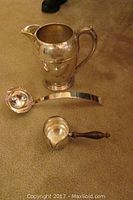Photo showing all three silver pieces together on carpet: pitcher, ladle, and small pourer with wooden handle.