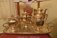 Photo showing 6 pieces of the silver plated coffee and tea set including the coffee pot (lid broken), teapot, sugar bowl, creamer, and waste bowl, placed on the serving tray.