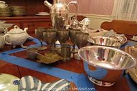 Overview of two Paul Revere reproduction bowls and assorted silver-tone tableware including pitchers and teapots on wooden table