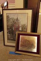 Two framed wall art pieces, one Damascene etching on metal and one watercolor print, resting against floor and mirror.