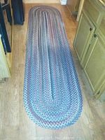 Long oval wool braided rug with mixed purple, blue, and cream colors on light wood floor.