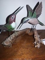Pair of hand-carved hummingbird wooden sculptures on a natural wood branch base, shown from the front.