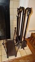 Photo showing 4 wrought iron fireplace tools with decorative handles and part of the stand