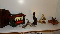Shelf displaying Goebel Tender Loving Care figure of child with cat, carved pelican figure, stained glass hummingbird, San Francisco style music box, and stained glass bird dish.