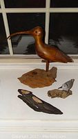 Four wooden bird carvings displayed on a surface: large shorebird on light wood base, single small bird on driftwood base, and two small birds on dark base.