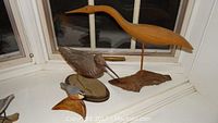 Photo showing all three carved bird sculptures together on a white windowsill: small nuthatch in front, mid-sized shore bird in the middle, and large heron behind.